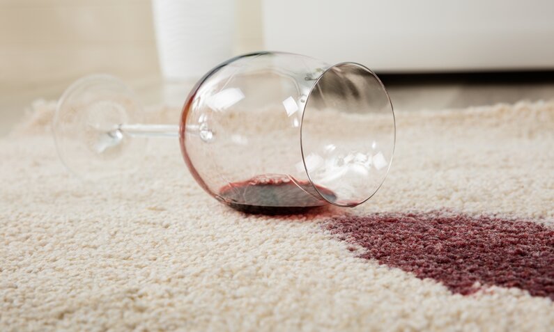 Ein Weinglas liegt seitlich auf einem beigen Teppich, neben einem sich ausbreitenden Wein-Fleck. | © Getty Images/ AndreyPopov
