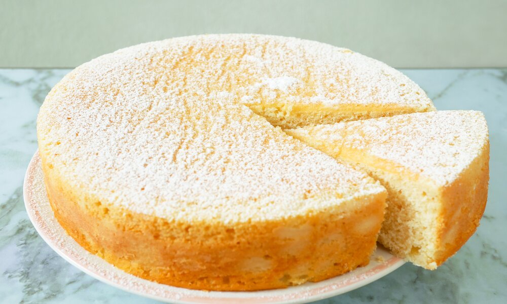 Angeschnittener Joghurtkuchen auf einem Kuchenteller mit Puderzucker. | © Getty Images / p_saranya