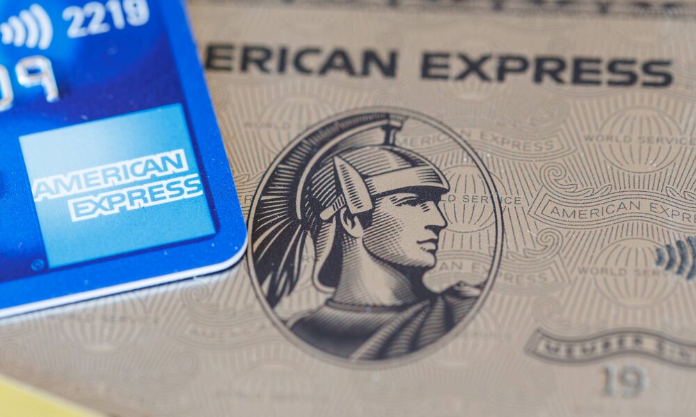 Ausschnitt einer blauen American Express-Karte, die auf einer platinfarbenen Karte mit dem markanten Centurion-Kopf liegt. | © IMAGO/Zoonar