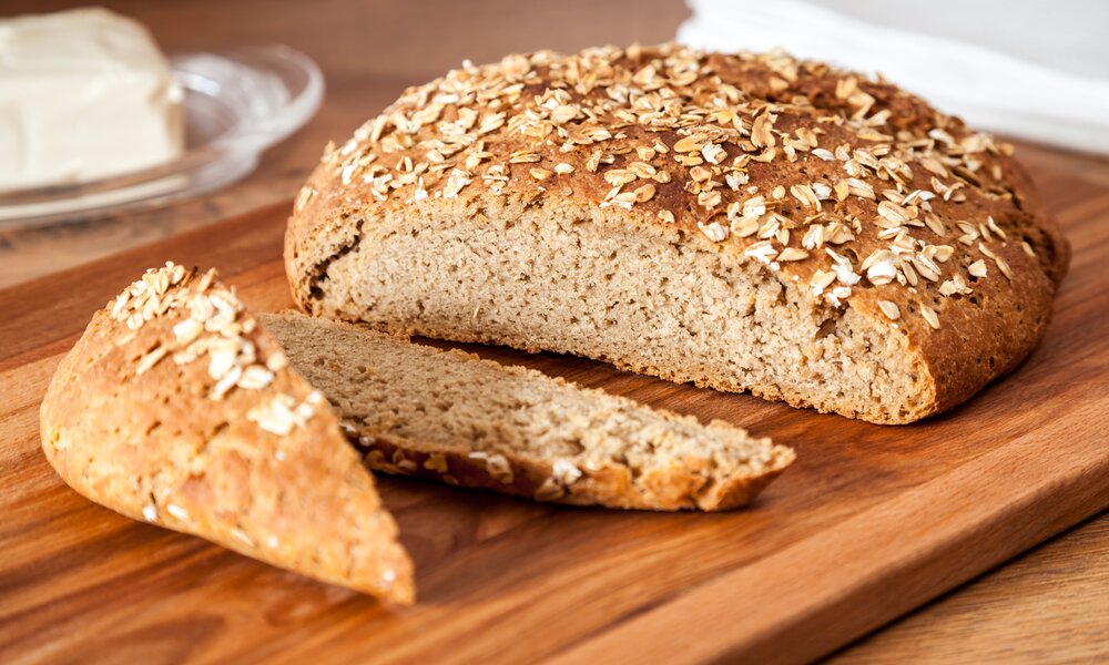 Angeschnittener Laib Haferbrot auf einem Holzbrett, dahinter Butter. | © Getty Images / Belyaevskiy