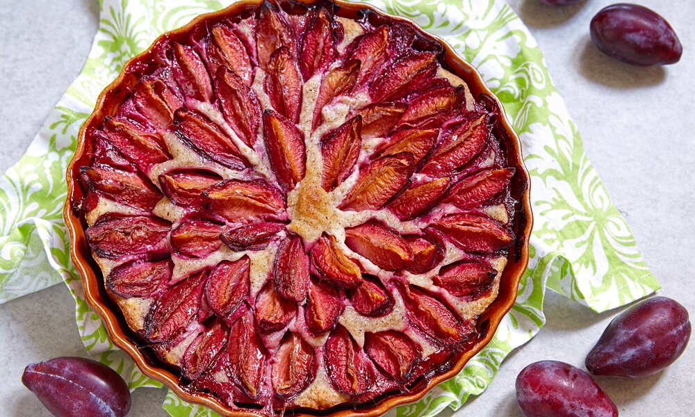 Zuckerfreier Pflaumenkuchen in einer Tortenform, daneben frische Pflaumen. | © Getty Images / Azurita