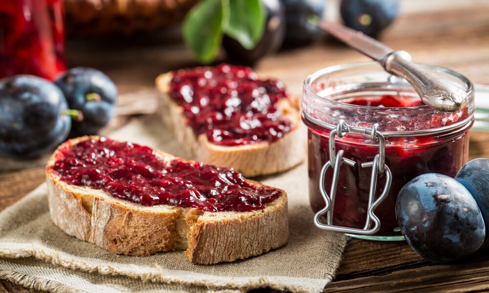Pflaumenmarmelade auf ein Graubrot geschmiert, daneben ein offenes Glasbehältnis mit Marmelade und frische Pflaumen daneben. | © Getty Images / Shaiith