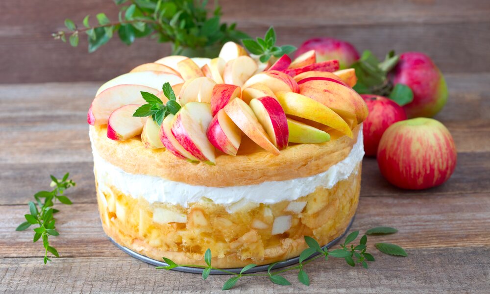 Apfel-Schmandkuchen mit getoppten frischen Apfelstücken auf einem Holzuntergrund angerichtet. | © Adobe Stock / rainbow33