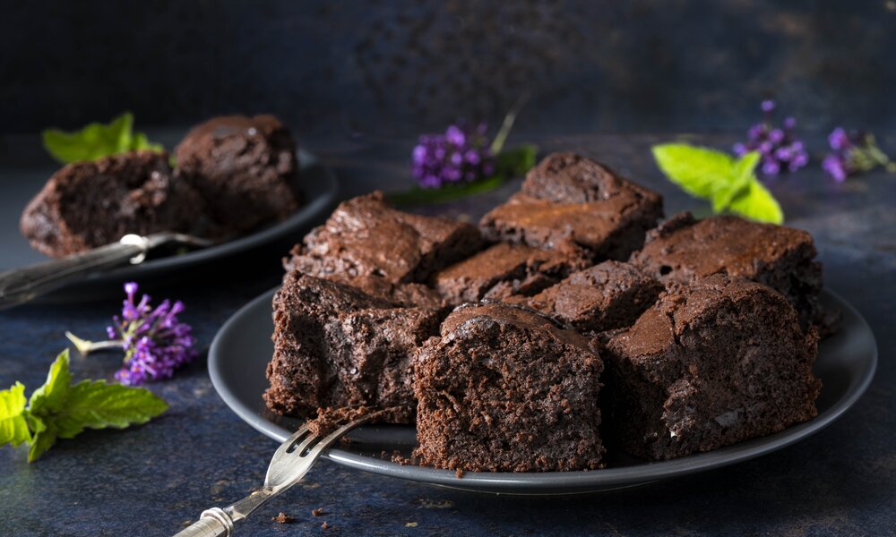 Einige Stücke Brownies auf einem Teller angerichtet, daneben frische Fliederblüten. | © Getty Images / ZAKmac