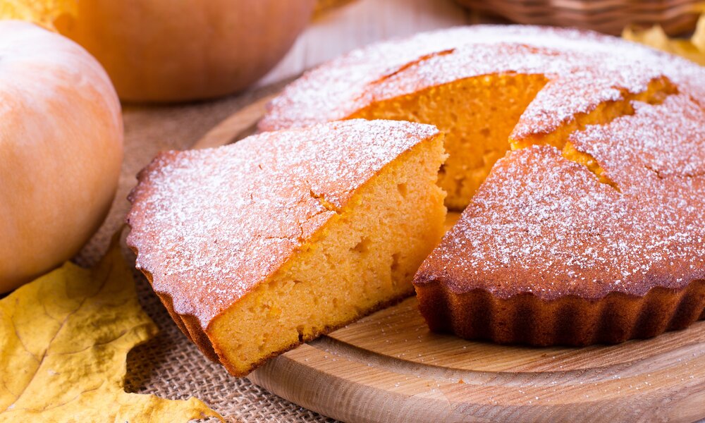 Angeschnittener Kürbis-Joghurtkuchen mit Puderzucker bestreut auf einem Teller. | © Adobe Stock / qwartm