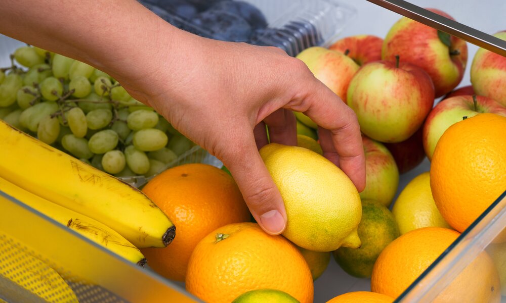 Eine Hand greift in eine Schublade voller bunter Früchte, darunter Zitronen, Bananen, Trauben und Äpfel. | © Adobe Stock/ rosinka79