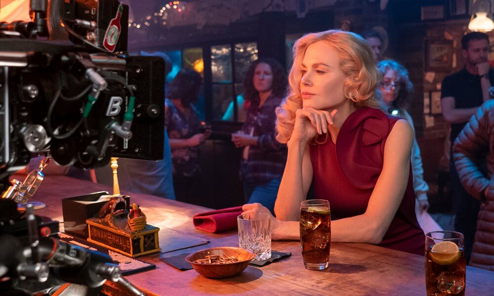 Auf einem Foto vom Dreh der Netflix-Serie "Ein neuer Sommer" sitzt Nicole Kidman draußen an einer Bar und wird von einer großen Kamera gefilmt. | © Netflix/Liam Daniel