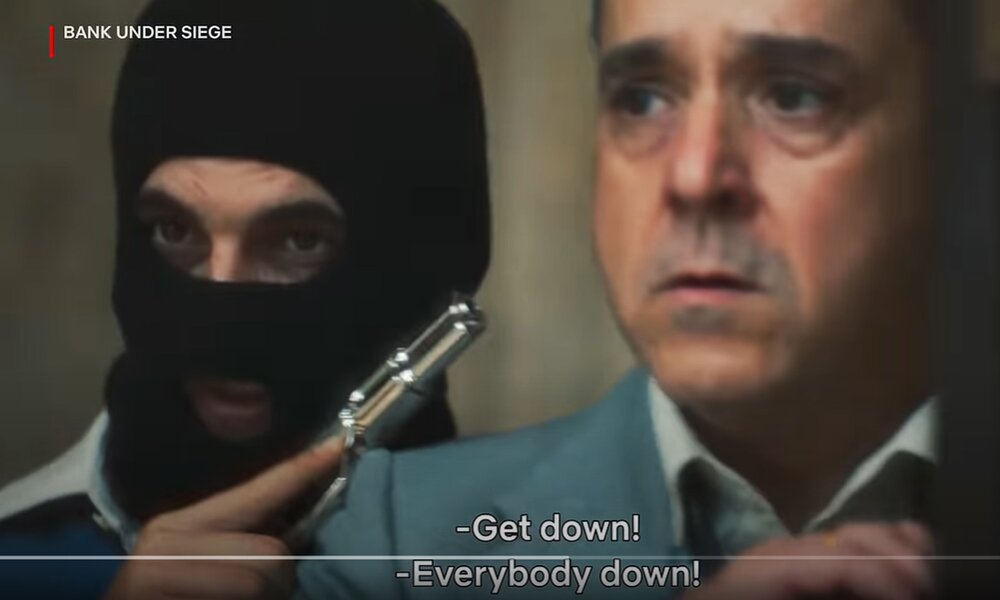 Maskierter Mann mit Waffe und eine Geisel in einer Szene aus dem Trailer zur Netflix-Serie "Bank under Siege" | © Ntflix