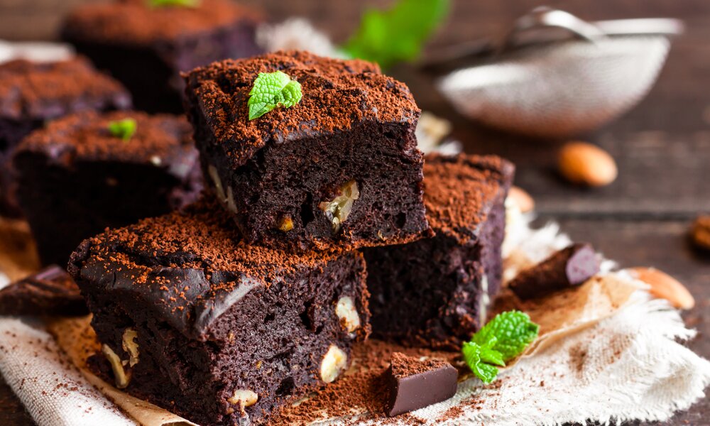 Mehrere gestapelte super saftigen Brownies auf einem Teller mit Kakaopulver bestreut. | © Adobe Stock / yuliiaholovchenko