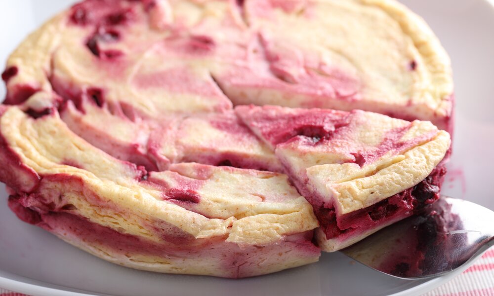 Angeschnittener Kirsch-Käsekuchen auf einem rosafarbenen Kuchenteller. | © Adobe Stock / StockphotoVideo