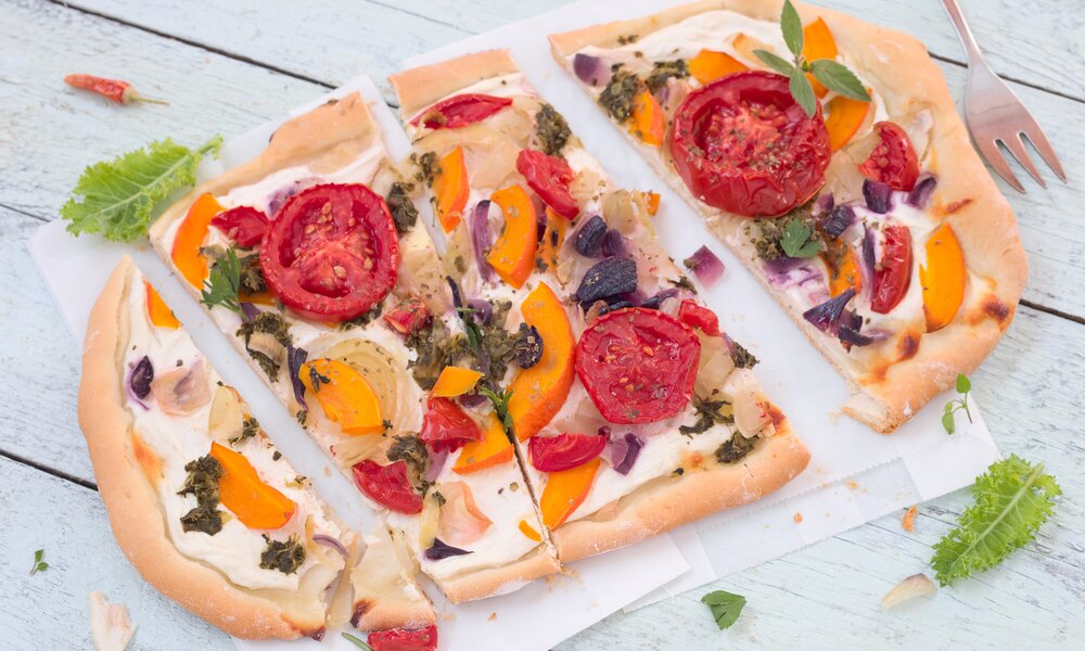 Pizza mit einem Belag aus Tomaten, Kürbis, Gewürzen und Pesto auf einem Backpapier auf einem Holzuntergrund. | © Adobe Stock /  rainbow33