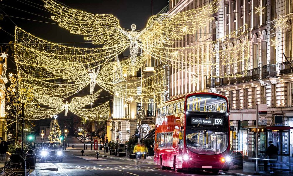 Ein roter Doppeldeckerbus fährt unter festlichen Engelslichtern und Weihnachtsdekorationen durch die abendliche Londoner Innenstadt. | © Alexey Fedorenko / stock.adobe.com