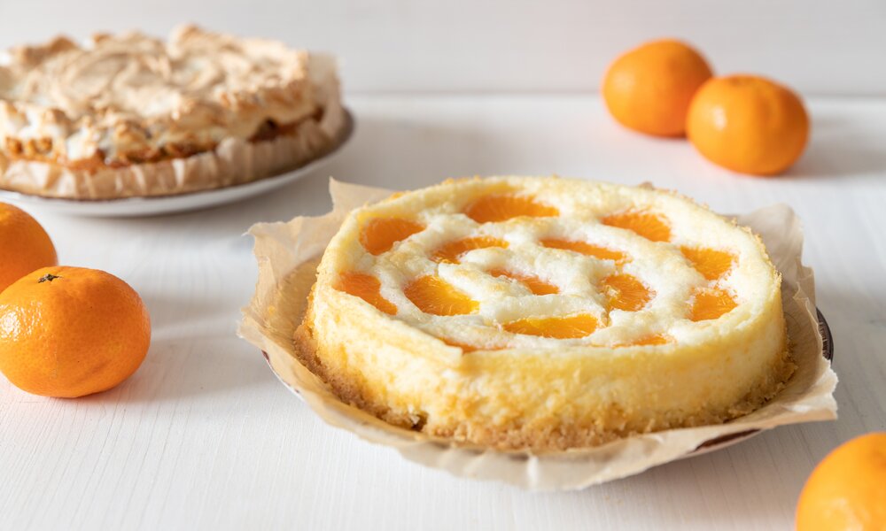 Cremiger Mandarinen-Käsekuchen auf einem Backpapier belegtem Teller. | © Adobe Stock / Kerstin