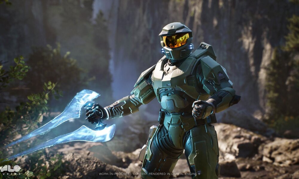 Ein gepanzerter Soldat in grüner Rüstung hält eine leuchtende Energiewaffe, während er in einer felsigen Waldlandschaft steht. | © Microsoft