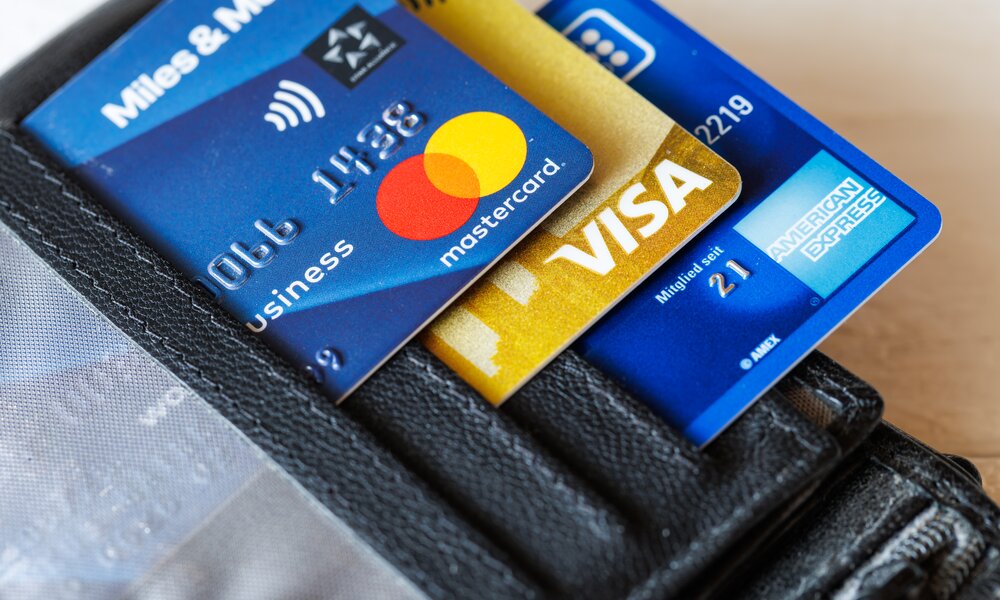 Drei Kreditkarten (Mastercard, Visa und American Express) stecken in einem schwarzen Lederetui auf hellem Hintergrund. | © IMAGO/Panthermedia