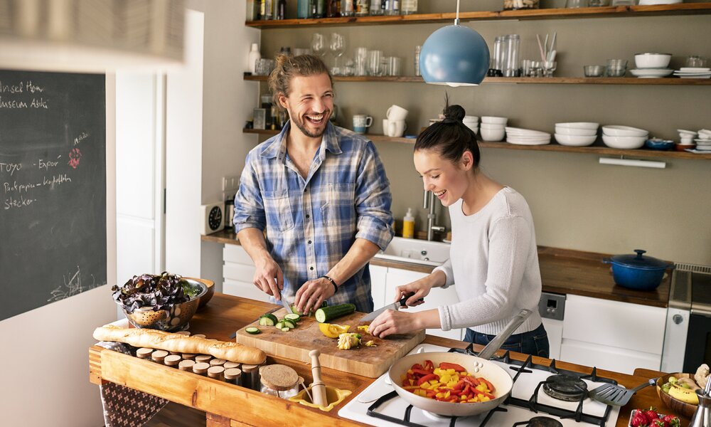Mann und Frau stehen in der Küche und kochen und lachen dabei. | © Getty Images / Westend61