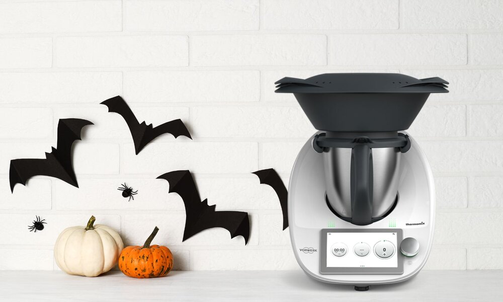 Halloween-Dekoration mit Kürbissen, Fledermäusen und Spinnen neben einem Thermomix auf einer weißen Arbeitsfläche. | © Adobe Stock/ Anna Khomulo/ Vowerk
