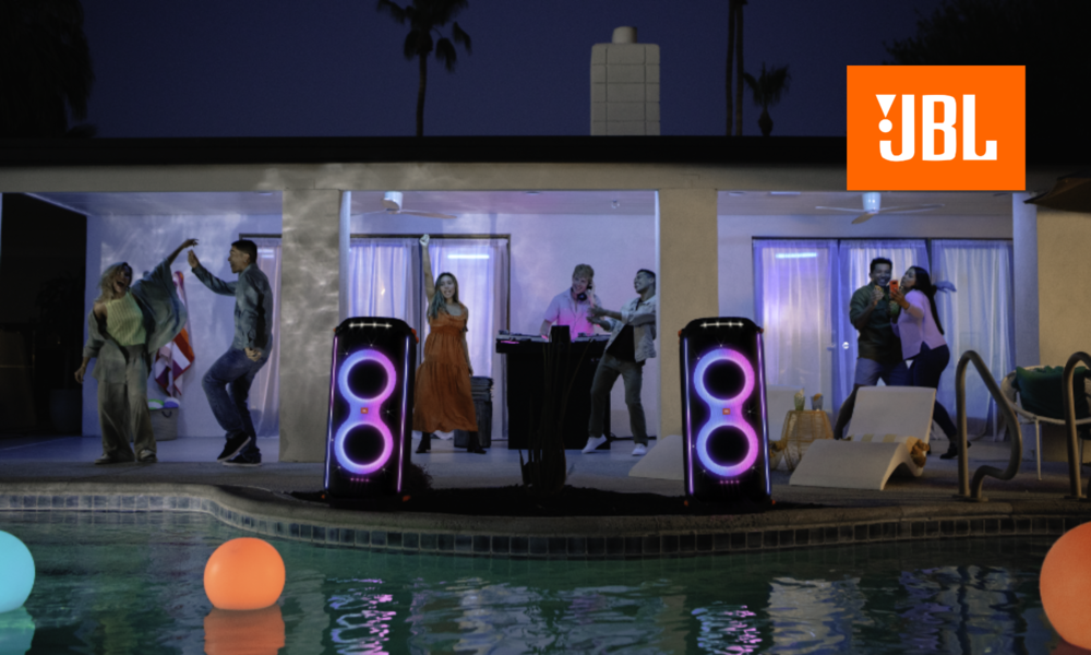 Junge Erwachsene tanzen ausgelassen im nächtlichen Garten vor beleuchteten JBL Partyboxen, während bunte Poollichter leuchten. | © Amazon/JBL