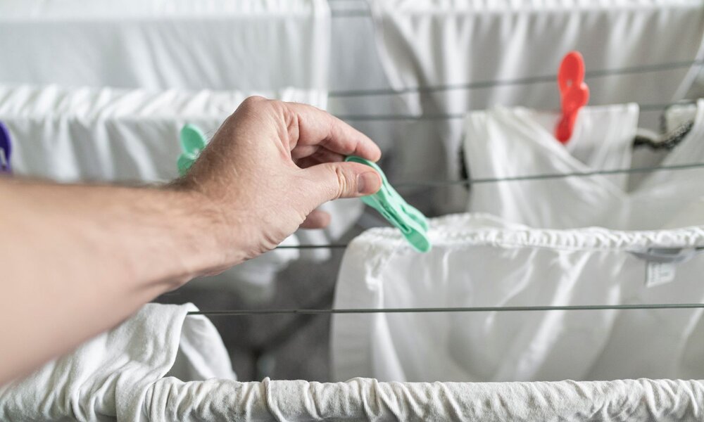 Eine Hand befestigt mit einer grünen Wäscheklammer ein weißes Kleidungsstück an einer Wäscheleine. | © Adobe Stock/ christophe papke
