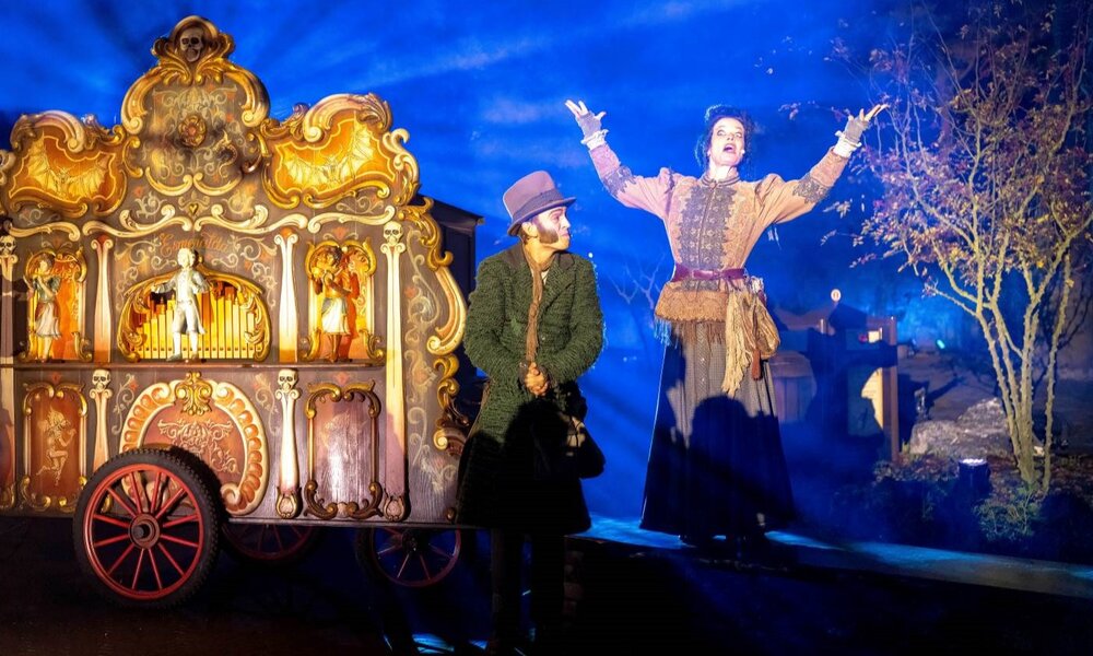 Eine Frau in viktorianischer Kleidung singt mit ausgebreiteten Armen neben einer dekorativen Drehorgel, während ein Mann in Mantel und Hut sie bewundernd ansieht. | © Efteling