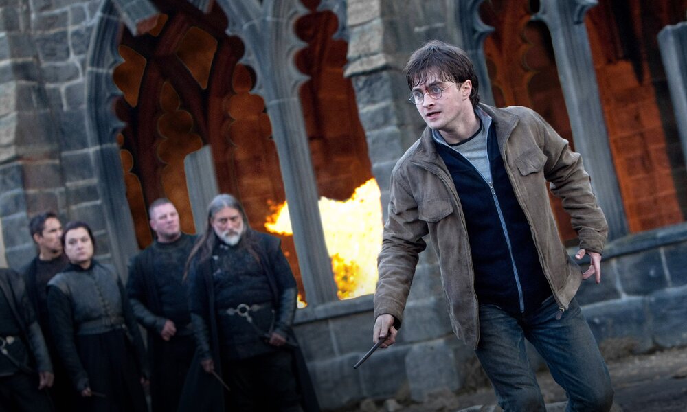 Daniel Radcliffe als Harry Potter steht mit Zauberstab in der Hand kampfbereit im Hof von Hogwarts, im Hintergrund einige schwarzgekleidete Männer. | © Imago Images/Warner Bros/Everett Collection
