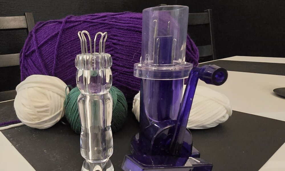 Eine durchsichtige Strickliesel und eine blaue Strickmühle stehen auf einem weißen Tisch vor bunter Wolle | © Sabrina Forst