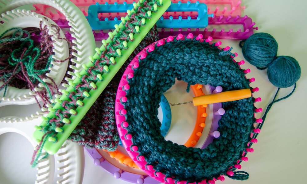 Bunte Strickringe, eine Stricknadel und zwei Wollknäuel in Blau und Grün liegen auf einem weißen Tisch. | © JMP Traveler / iStock / Getty Images Plus 
