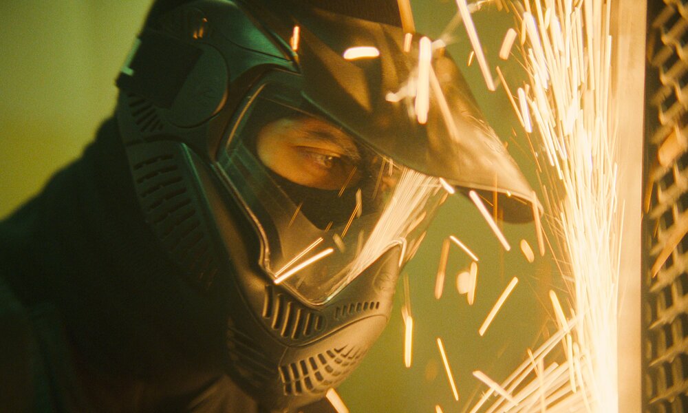 Funken fliegen in der Nahaufnahme eines Mannes  mit Maske und Schweißgerät in einer Szene aus der Netflix-Serie "Der Helikopter Coup" | © Netflix