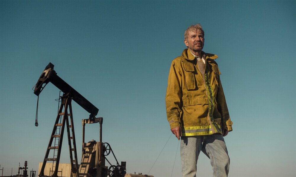 Billy Bob Thornton steht in einer Szene aus der Paramount+-Serie "Landman" in Schutzjacke unter blauem Himmel vor einem Ölbohrturm. | © Paramount+
