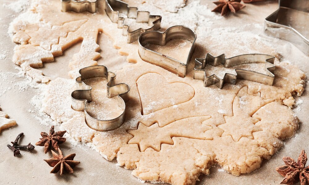 Roher Keksteig auf einer Arbeitsplatte, Ausstecher in Weihnachtsmotiven in den Teig gedrückt. | © matttilda