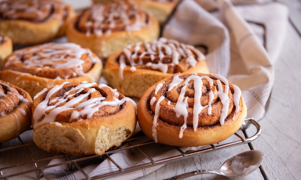Mehrere Zimtschnecken auf einem Kuchengitter mit Zuckerguss bezogen. | © Adobe stock / Maresol