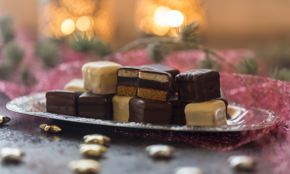 Mehrere Dominosteine auf einem Teller in weihnachtlicher Umgebung. | © Getty Images / Westend61
