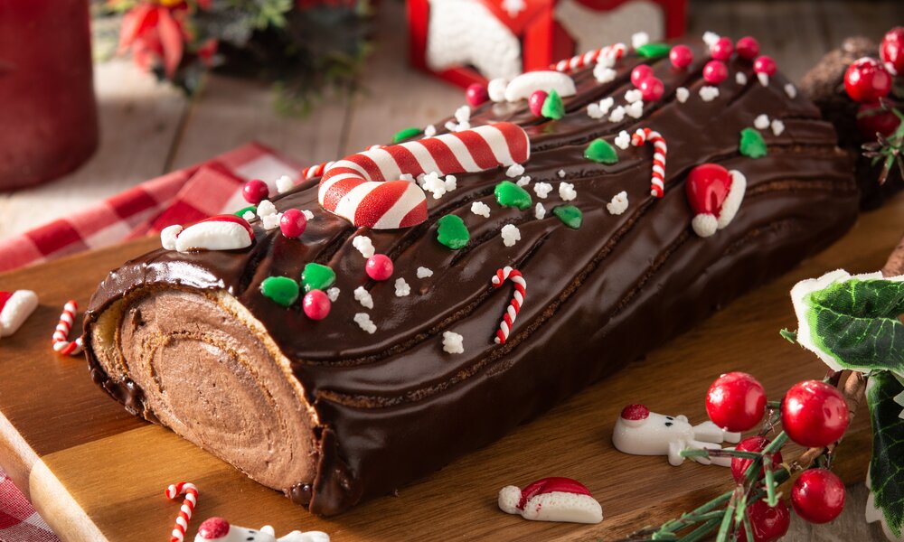Weihnachtlich dekorierte Schokoladen-Biskuitrolle auf Holzbrett. | © Adobe Stock / chandlervid85