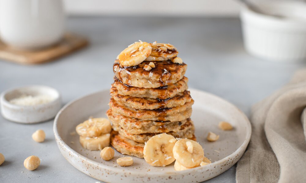 Gestapelte Pancakes aus Haferflocken mit Bananen, Nüssen und Sirup. | © Adobe Stock / Mila Naumova