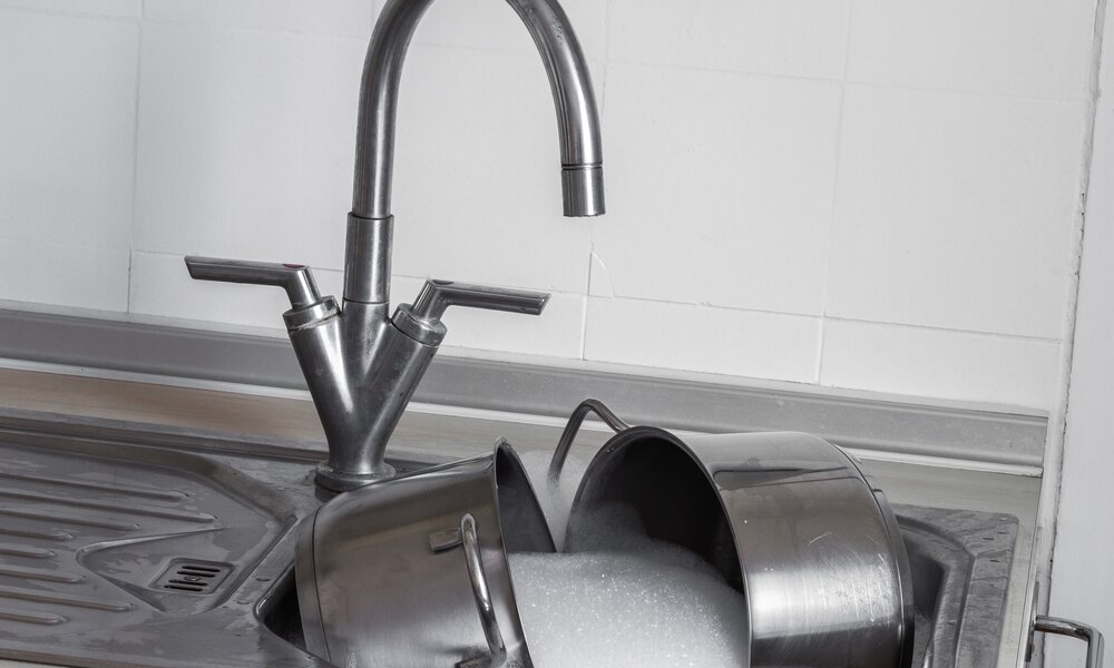Eine silbernes Waschbecken in der Küche mit laufendem Wasser, in der Spüle liegen Töpfe in einem Schaumbad | © Adobe Stock/blende11.photo