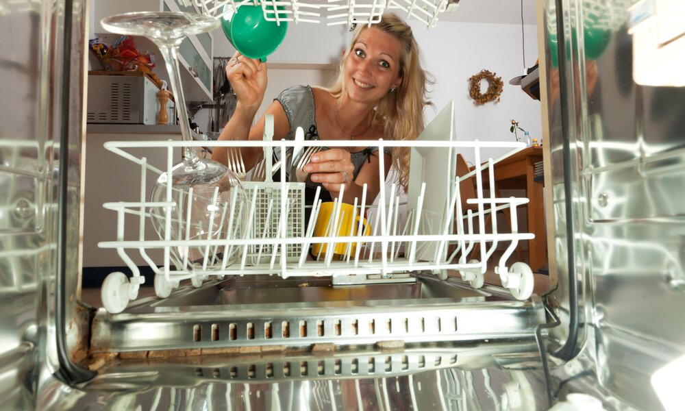 Spülmaschine von innen, am Ende der Spülmaschine sitzt ein blonde Frau, die gerade die Spülmaschine einräumt, in der Maschine sind einige Teller usw. | © Adobe Stock/Bernd Jürgens