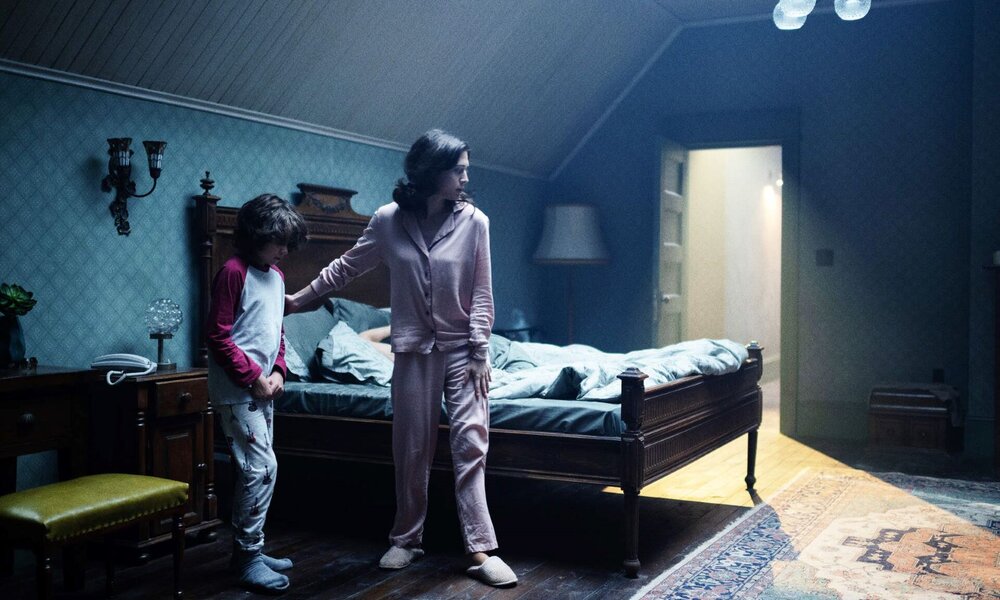 Eine Frau in rosa Pyjama beruhigt einen Jungen im Schlafanzug in einem düsteren Schlafzimmer mit Holzboden und antikem Bett. | © Tobis Film GmbH