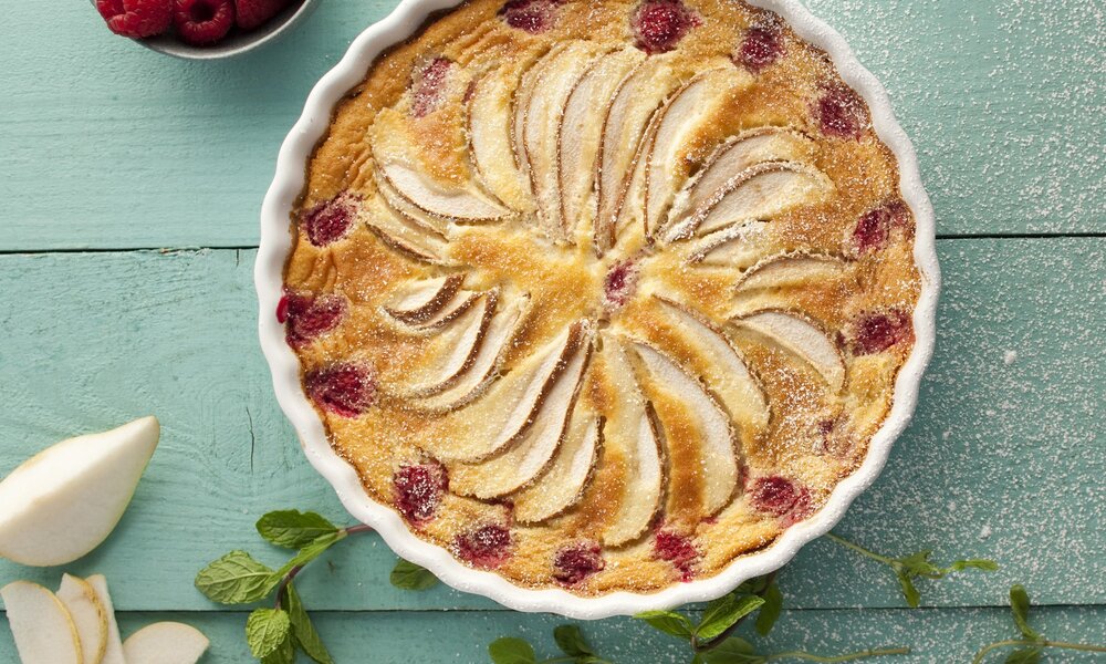 Birnen-Himbeer-Kuchen von oben in einer weißen Kuchenform auf einem Tisch angerichtet. | © Getty Images / 	Portugal2004
