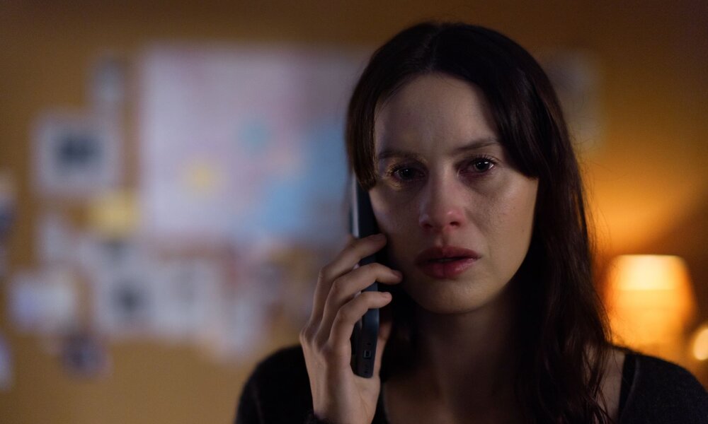 Eine junge Frau mit langen dunklen Haaren und geröteten Augen hält ein Telefon ans Ohr und blickt traurig in einem schwach beleuchteten Raum. | ©  Cr. Julio Vergne/NETFLIX © 2024