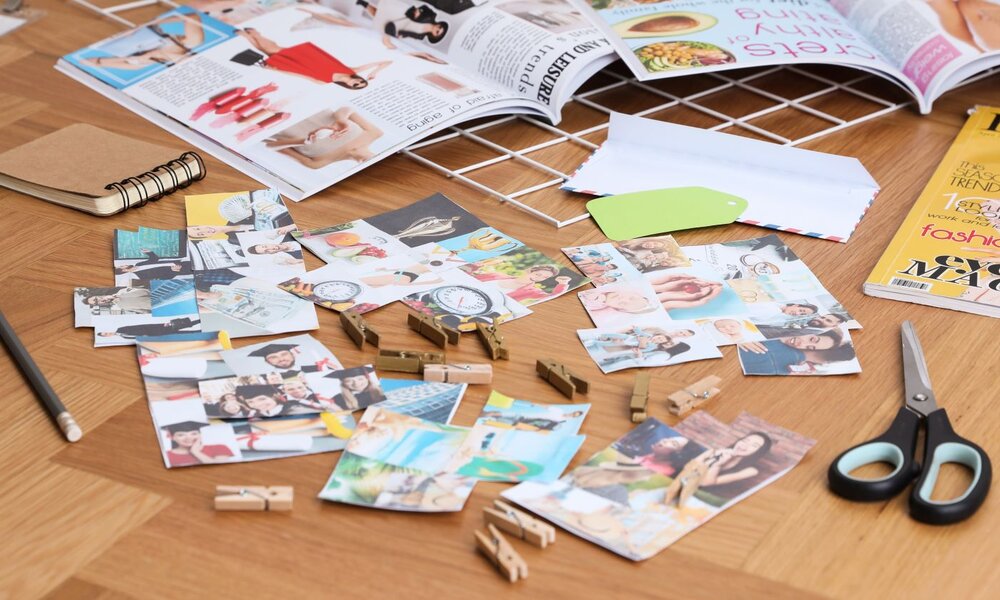Bunte Collagenfotos und Zeitschriftenseiten auf Holzuntergrund, umgeben von Bastelmaterialien wie Notizbuch und Schere. | © New Africa / stock.adobe.com