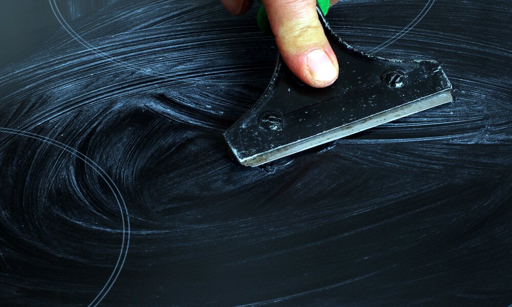 Glaskeramikkochfeld in schwarz, eine männliche Hand scharbt mit Scharber ein weißes Reinigungsmittel darüber  | © Adobe Stock/Osterland
