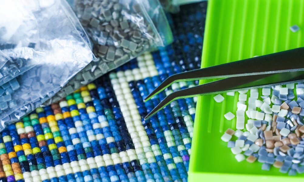 Nahaufnahme eines Mosaikprojekts mit bunten Steinchen, einer grünen Sortierschale, Pinzette und Plastiktüten im Hintergrund. | © ANGHI /stock.adobe.com