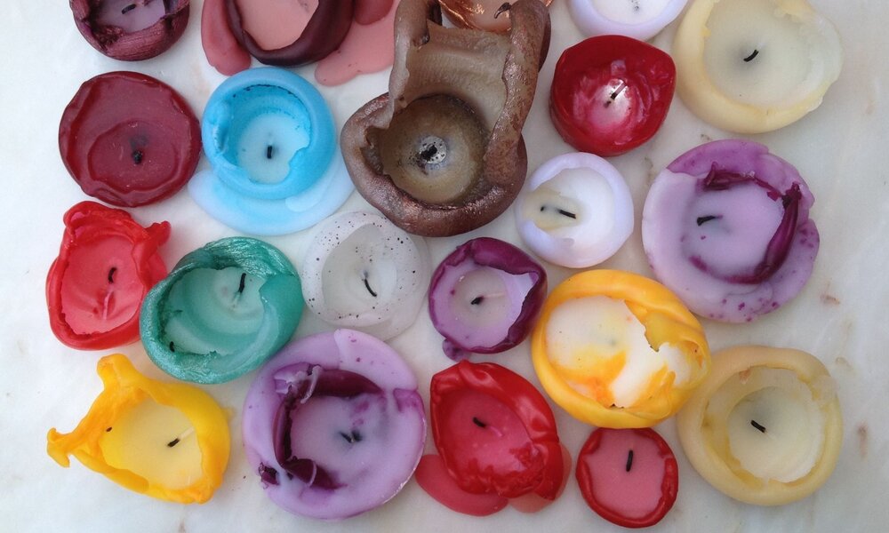 Bunte, teils geschmolzene Teelichtreste in verschiedenen Farben liegen chaotisch auf einer hellen, marmorierten Oberfläche. | © maerzkind / stock.adobe.com