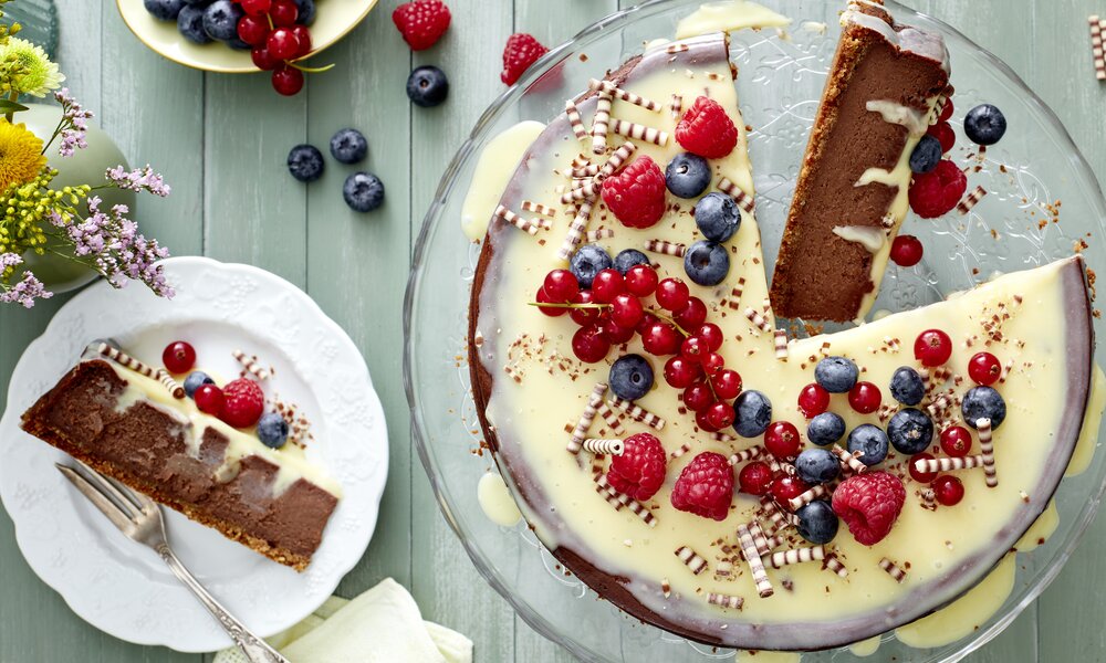 Angeschnittener Schoko-Käsekuchen belegt mit frischen Beeren in bunter Umgebung angerichtet. | © Isabell Triemer