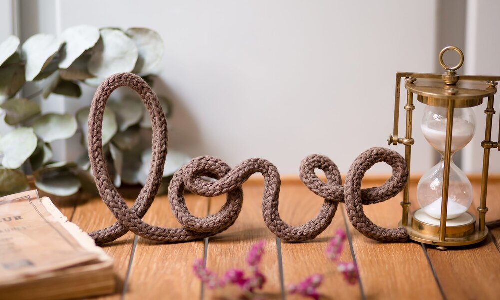 Schriftzug "love" aus braunem Seil auf Holzuntergrund, daneben eine goldene Sanduhr und Eukalyptusblätter im Hintergrund. | © Nastasia Froloff /stock.adobe.com 