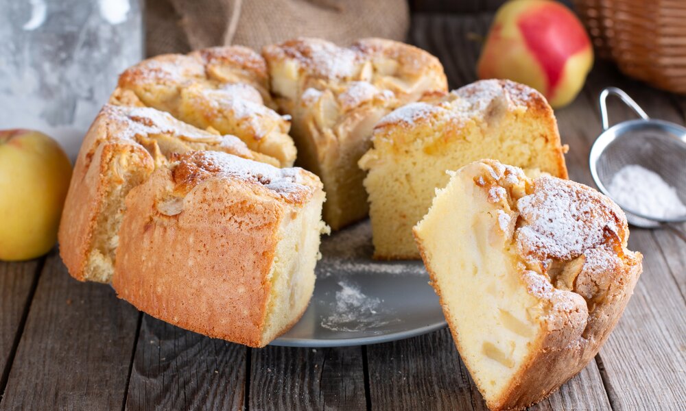 In Stücke geschnittener Apfel-Rührkuchen auf einem Teller angerichtet, mit Puderzucker bestreut. | © Getty Images / Qwart