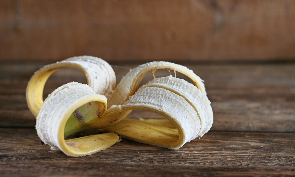 Eine leere Bananenschale mit gelber Außenseite und heller Innenseite liegt auf einem rustikalen Holztisch. | © Adobe Stock/ Alena Bogdanova