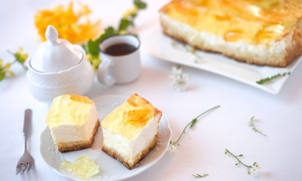 Zwei Stücke Mandarinen-Schmandkuchen auf einem Teller, dahinter der ganze Kuchen. | © Adobe Stock /  rainbow33