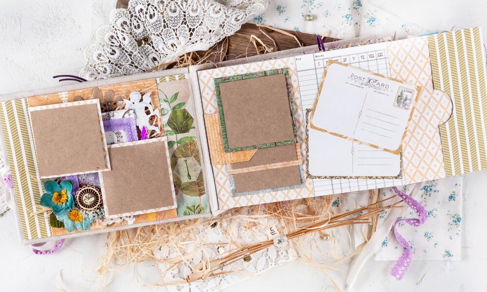 Ein kunstvoll gestaltetes Scrapbook mit Vintage-Elementen, Stoffblumen und Spitzenband liegt offen auf einer weißen Oberfläche mit Holzelementen. | © Svetlana Glazkova/stock.adobe.com