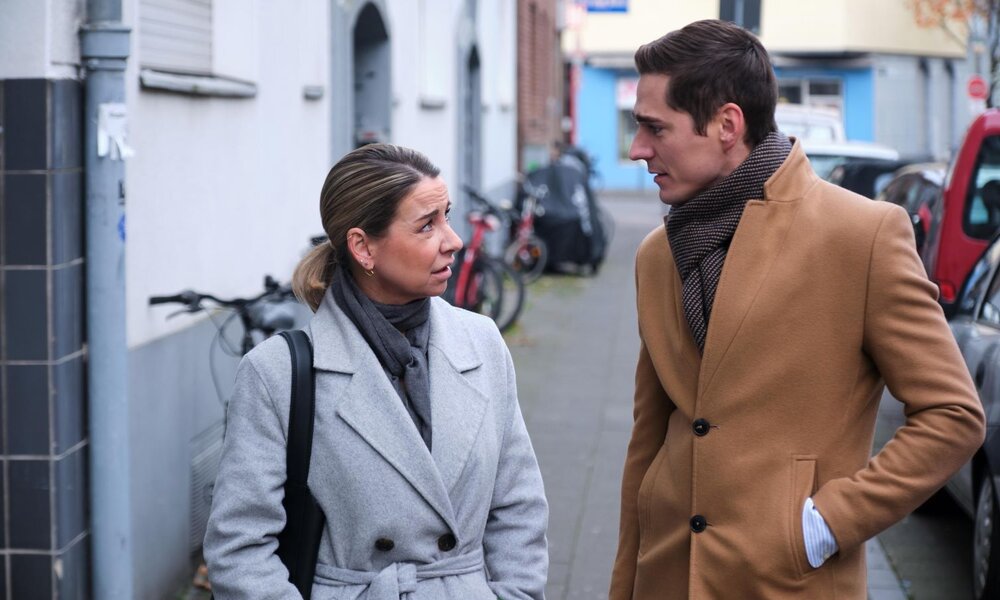 Zwei Menschen im Wintermantel sprechen auf einem Gehweg, die Frau blickt skeptisch, der Mann hat eine Hand in der Tasche. | © RTL / Stefan Behrens